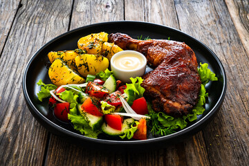 Oven roasted chicken thigh with boiled potatoes and fresh vegetables on wooden table
