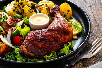 Oven roasted chicken thigh with boiled potatoes and fresh vegetables on wooden table
