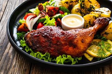 Oven roasted chicken thigh with boiled potatoes and fresh vegetables on wooden table
