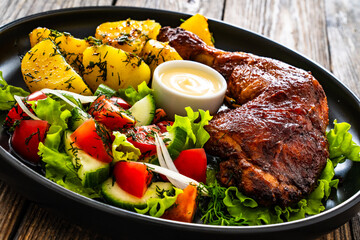 Oven roasted chicken thigh with boiled potatoes and fresh vegetables on wooden table
