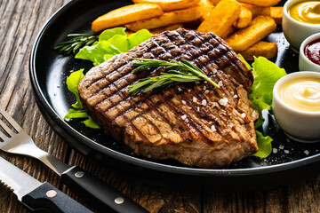 Grilled beef sirloin steak with French fries on wooden table
