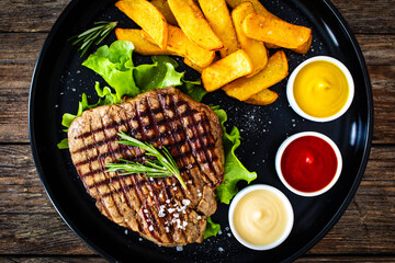 Grilled beef sirloin steak with French fries on wooden table

