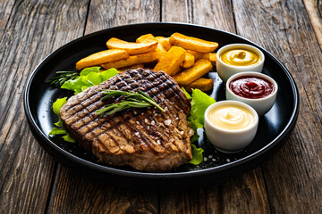 Grilled beef sirloin steak with French fries on wooden table
