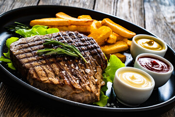 Grilled beef sirloin steak with French fries on wooden table
