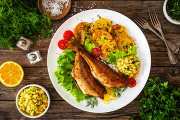 Fried sea bass with fried potatoes and fresh cabbage salad on wooden table

