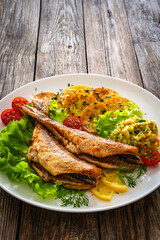 Fried sea bass with fried potatoes and fresh cabbage salad on wooden table

