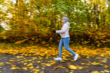 Motion Blur.  Mid-adult woman blurred silhouette exercising Nordic walking in city park 
