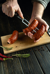 Grilled sausages on a fork in the hands of a cook. The concept of cooking sausages by the hands of...