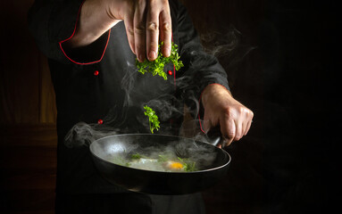 Cooking eggs in a frying pan. An experienced chef throws fresh parsley into a frying pan with an egg. Space for advertising on a black background.