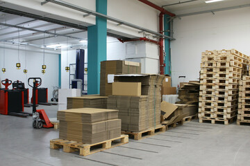 An image of a room with stacked wooden pallets, cardboard packaging, and equipment for transporting...