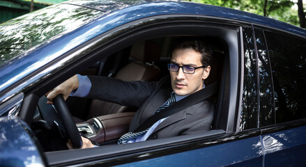 Handsome businessman in black suit driving in luxury car	