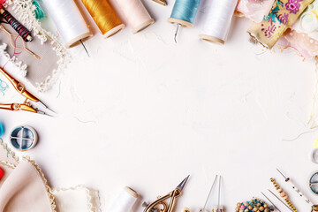 Photo in light elegant tones of different fabric and sewing tools, sewing accessories, sewing threads, thread spools, needles, pins on the white table with copy space - obrazy, fototapety, plakaty