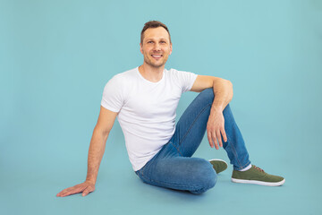 Handsome young bearded man sitting and smiling at camera isolated on blue background.