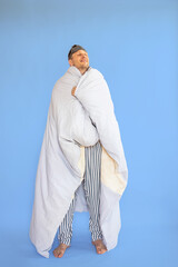 Full body young man wearing pyjamas jam sleep eye mask wrapped in blanket duvet rest relax at home...