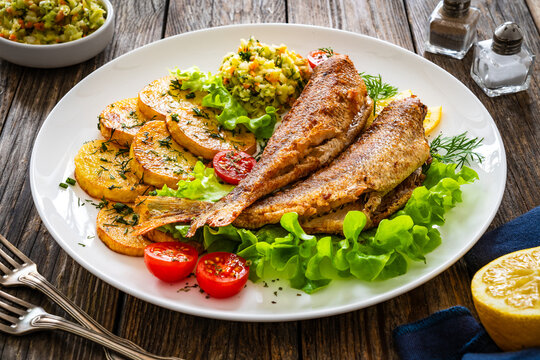 Fried sea bass with fried potatoes and fresh cabbage salad on wooden table

