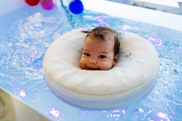 Small child or a baby is swimming and having a pleasant time during a physical therapy session in the pool. Baby is looking at camera and smiling.