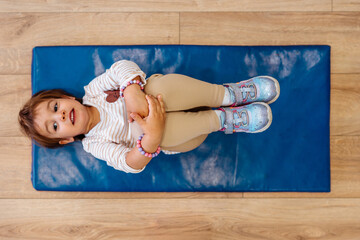 Adorable young girl enjoying in her physical therapy sessions, playing contentedly in a children's gym designed for therapeutic activities. She happy and lies on an exercise mat. View from above.
