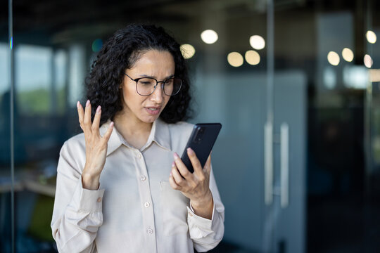 Upset thinking business woman close up inside office, young hispanic woman reading bad news on phone online, business woman at workplace holding smartphone typing text message