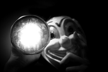 Creepy clown carrying flashlight in the dark