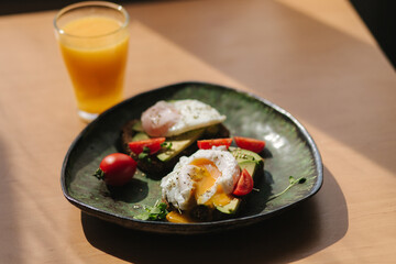 Sandwiches with avocado eggs and tomatoes. Healthy and tasty breakfast on green handmade plate. Fresh orange juice