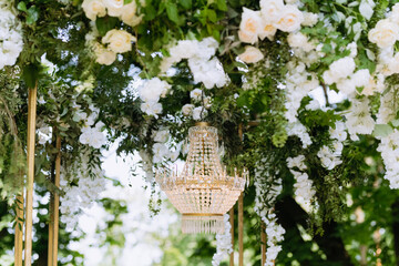 Vintage chandelier on the wedding arch. a close-up of a crystal chandelier hangs over a green photo...