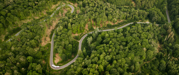 Aerial view of the winding Road going over the mountain and through the forest, with truck and trailer in the curve
