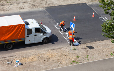 Summer road works. A team of road workers in orange safety signal vests apply markings to a Speed...