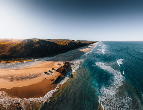 K'gari High angle aerial bird's eye drone view of the Maheno shipwreck on Seventy-Five Mile Beach on Fraser Island, Queensland, Australia. Beautiful sunset light with waves.