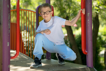 Fototapeta premium A little boy in a white T-shirt and glasses. A boy on a playground for children. A cheerful boy. Baby model.
