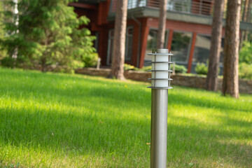 Modern silver lamp post on lush green lawn with charming wooden house in background