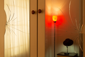 Broken mirrors on the wardrobe door. Reflection of a tulle curtain, a red lampshade and a man's hat...