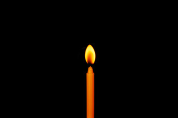 A yellow candle burns isolated on a black background.