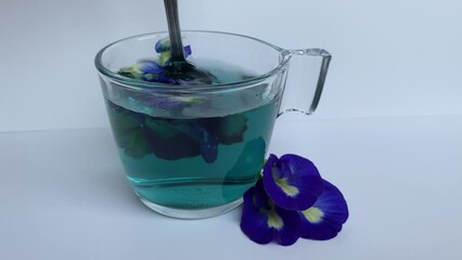 Spoon stiring of  butterfly pea flower tea, or Clitoria ternatea. Inside transparent glass, isolated on white background. Time lapse diffusion 