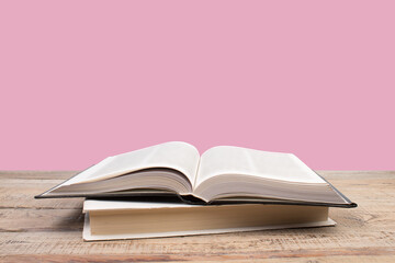 open book. Composition with hardback books, fanned pages on wooden deck table and pink background....