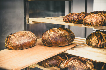 Freshly baked bread is pushed into a shelf cart in a bakery using a wooden pusher - obrazy, fototapety, plakaty