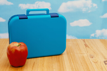 Lunchbox with apple on wood desk with the sky