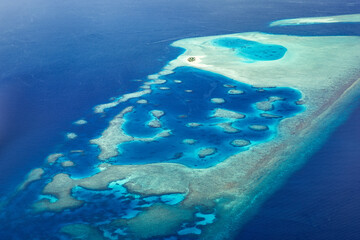 Aerial view or top view of tropical island beach with clear water coral reef. Maldives atolls, nature paradise. Shades of blue, relaxing aerial seascape, landscape. Sunny exotic travel background