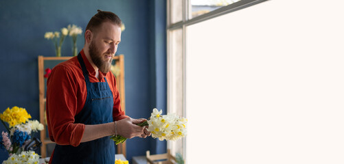 Male florist creating a bouquet of spring flowers while standing in his flower shop. Concept of...