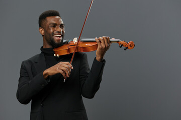 Elegant African American man in black suit playing violin on gray background in studio setting