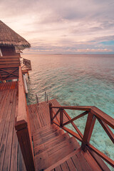 Perfect sunset on Maldives island, luxury water villas resort and wooden pier. Beautiful cloudy sky...