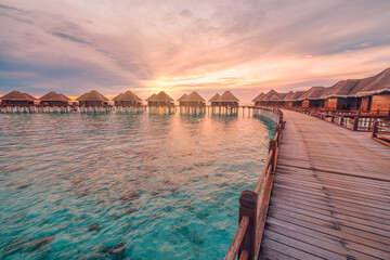Perfect sunset on Maldives island, luxury water villas resort and wooden pier. Beautiful cloudy sky...