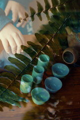 Manos sostienen copas de té, doble exposición con plantas verdes naturales