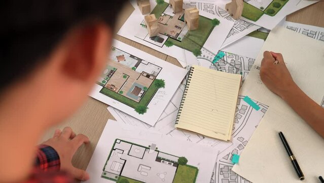 Architect and engineer consider or discuss about building construction using blueprint on table with architectural document, measurement tool and wooden block scatter around at office. Delineation.
