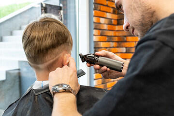 the process of cutting a blond boy with a long braid in a chair in a barbershop salon, a barbershop...
