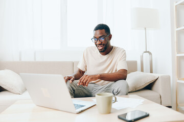 Smiling African American Freelancer Working on Laptop in Modern Home Office Young African American man sitting on a comfortable sofa in a modern living room, typing on his laptop With a relaxed and