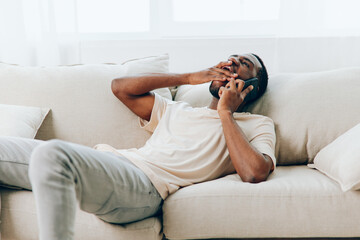 African American man on a black sofa, happily talking on his phone while video calling He is holding the phone with confidence, connecting with others in the comfort of his modern apartment With a