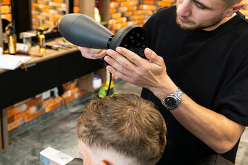 The picture of a professional barber is with a hair diffuser that he uses to make curly hair of a...