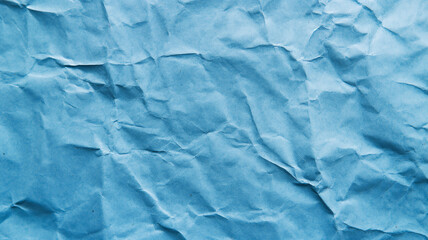 A close-up of a crumpled blue paper texture, showing intricate folds and creases across a vivid blue background.