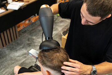 Barber drying his client's freshly treated hair with a blow dryer.