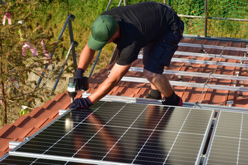 Dachdecker beim Aufbau einer Photovoltaikanlage auf einem neu gedeckten Ziegeldach: Verschraubung...